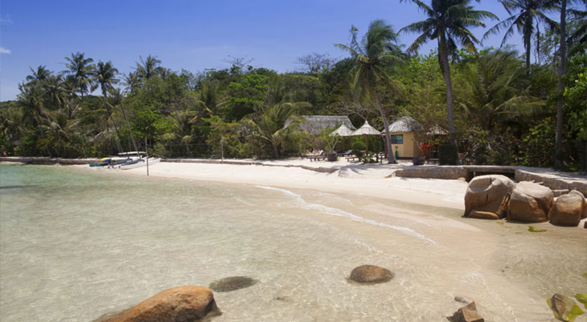 Tropisch zandstrand in Vietnam met palmbomen, helder zeewater en strandhuisjes aan de kust.