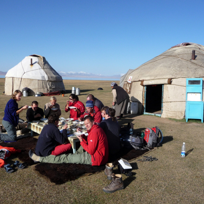 Groepsrondreis Kirgistan: reizigers lunchen bij een yurtkamp in de steppe, met bergen op de achtergrond.