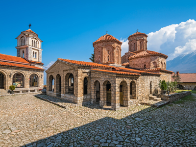 Kloostercomplex met stenen kerk en rode daken in Noord-Macedonië, met bergen op de achtergrond.