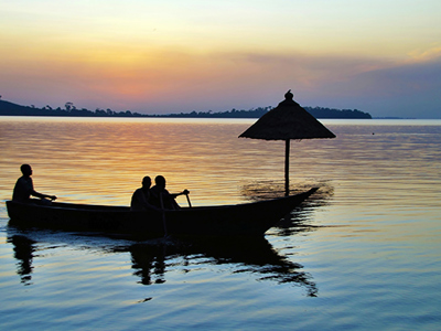Boot met drie mensen op het Victoriameer bij zonsondergang, onderdeel van de Route Oeganda.