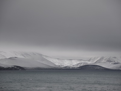 Besneeuwde bergen langs de kust van Antarctica, gezien vanaf zee onder een grijze lucht.