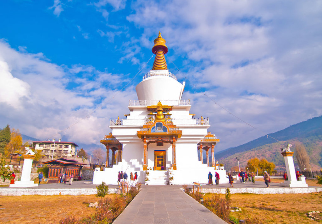 Witte boeddhistische stupa in Bhutan met gouden toren, tegen de Himalaya en blauwe lucht.