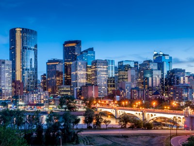Skyline van Calgary bij schemering met verlichte brug over de Bow River, Route Canada dag 1.