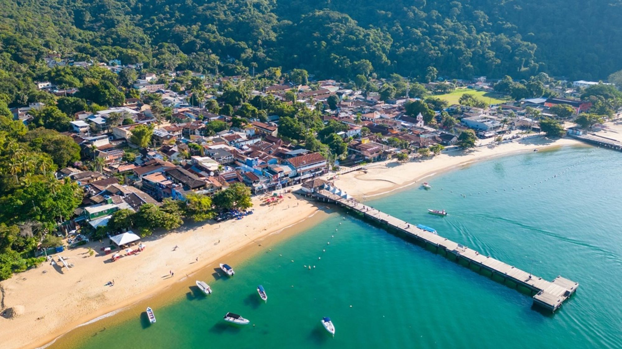een strandplaats in Brazilië met pier, turquoise zee en boten, omringd door groen.