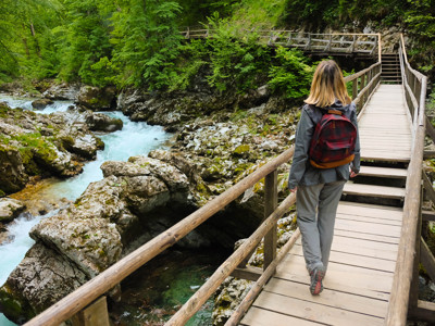 Wandelaar met rugzak op houten brug langs een turquoise rivier in een groene kloof in Slovenië.