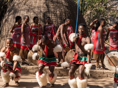 Traditionele dansvoorstelling in Zuid-Afrika met dansers in kleurrijke kleding voor rieten hutten.