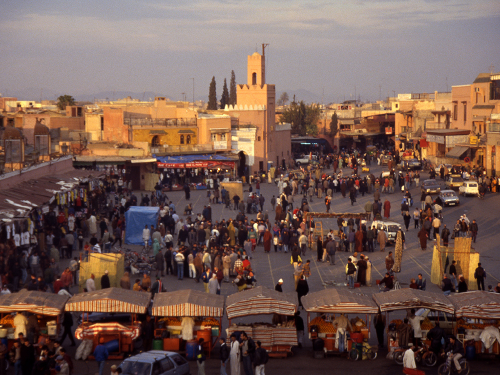 Drukke Djemaa el Fna in Marrakech met marktstalletjes en minaret, hoogtepunt van een groepsrondreis Marokko.