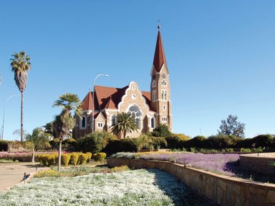 Christuskirche in Windhoek, Namibië, met palmbomen en bloeiende tuinen onder een heldere blauwe lucht.