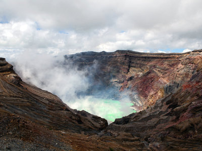 Krater van de vulkaan Aso met opstijgende stoom en felgroen kratermeer, Japan.