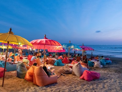 Strandcafé op Bali bij zonsondergang met kleurrijke parasols en zitzakken aan zee.
