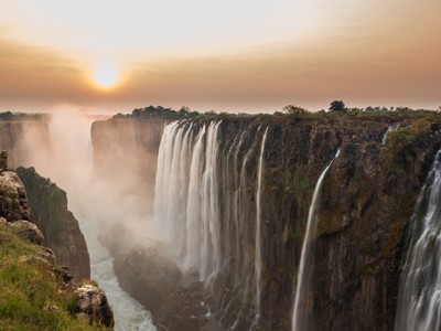 Zonsopkomst bij Victoria Falls met nevel boven de kloof en watervallen langs de rotswand.