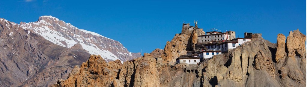 Boeddhistisch klooster op rotsen in Ladakh, met besneeuwde bergtoppen op de achtergrond.