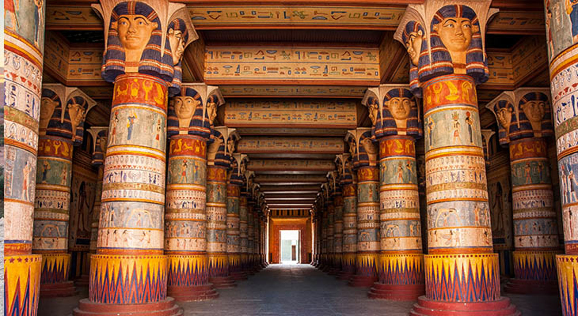 Rij kleurrijke zuilen met faraokoppen en hiërogliefen in een Egyptische tempelhal.