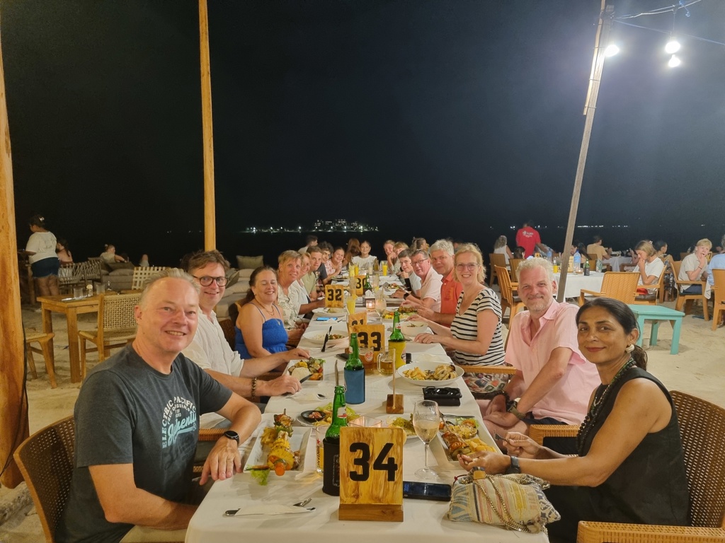 Reisgroep dineert aan lange tafel in strandrestaurant bij avond, Familiereis Kleine Sunda Eilanden.