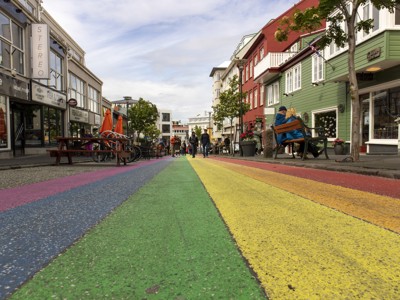 Regenbooggekleurde straat in Reykjavik met kleurrijke huizen, terrasjes en wandelaars.