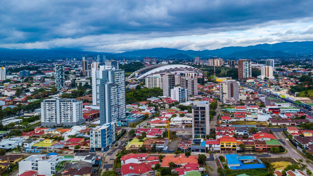 Skyline van San José, Costa Rica, met moderne hoogbouw en bergen onder een dreigende wolkenlucht.