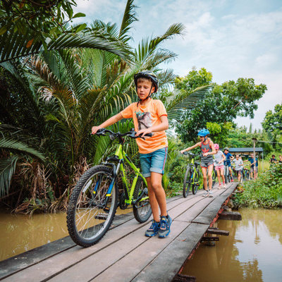Kinderen fietsen over een houten brug door tropisch groen tijdens familiereis Thailand Hoogtepunten.