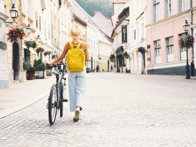 Fietser met gele rugzak loopt met haar fiets door een sfeervolle straat in Slovenië tijdens een fietsvakantie.