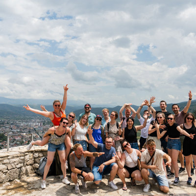 Groep 22-35ers reizigers poseert bij een uitzichtpunt met bergen en stad in Albanië.