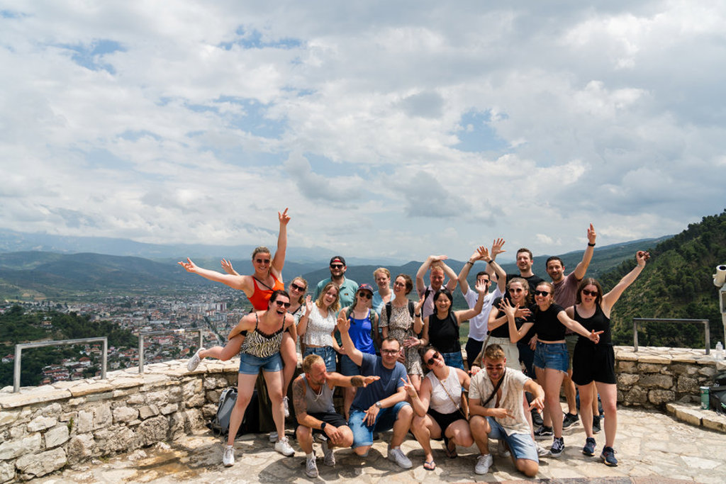 Groep 22-35ers reizigers poseert bij een uitzichtpunt met bergen en stad in Albanië.
