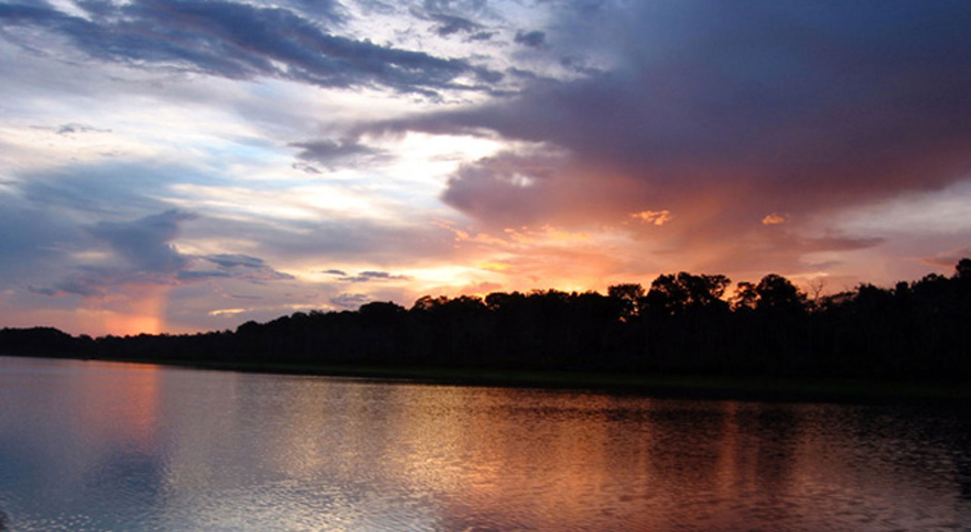 Zonsondergang boven een rivier met silhouetten van bomen en kleurrijke wolkenlucht in Colombia.