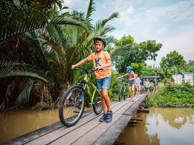 Fietstocht met kinderen over een houten brug tussen tropisch groen tijdens de route Thailand Noord en Zuid.