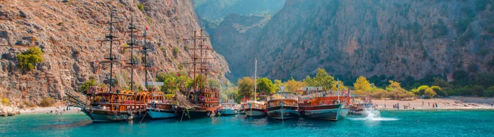 Uitzicht op Butterfly Valley in Turkije met turquoise zee, strand en aangemeerde boten tussen hoge rotskliffen.