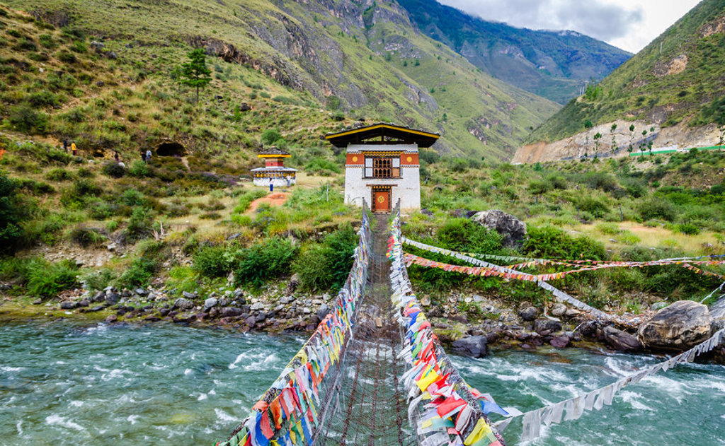 Hangbrug met gebedsvlaggen over een rivier in Bhutan, tijdens groepsrondreis Sikkim en Bhutan.
