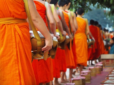 Monniken in oranje gewaden in een rij tijdens de ochtendronde met offergaven in Thailand.