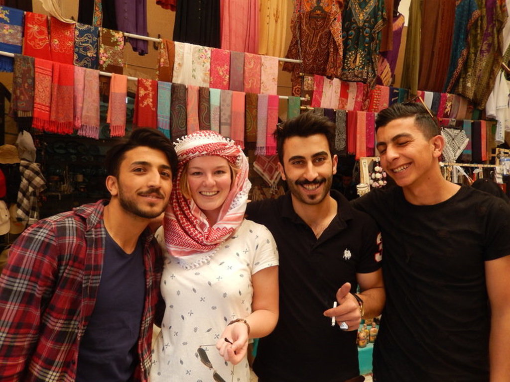 Reizigers tijdens een groepsrondreis Jordanië poseren in een kleurrijke souk met sjaals op de achtergrond.