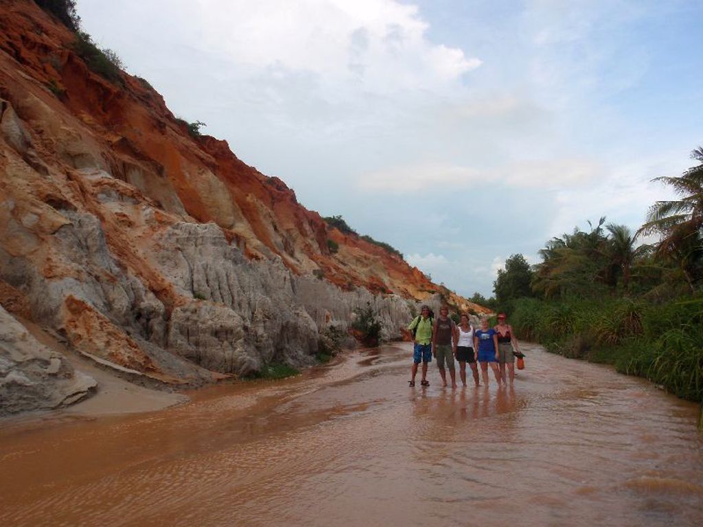 Gezin wandelt door een ondiepe rivier langs rode zandduinen in Vietnam tijdens een familiereis.