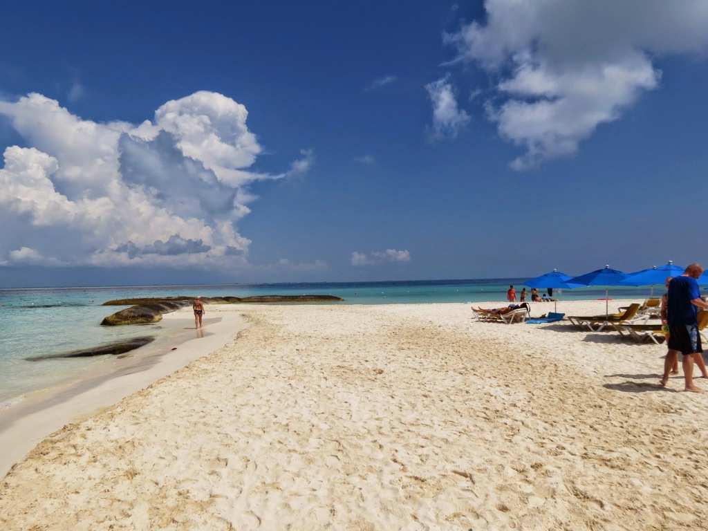 Wit zandstrand aan de Caribische kust van Mexico met ligbedden en parasols onder een blauwe lucht.