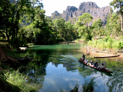 Boottocht op de Nam Song-rivier bij Vang Vieng, Laos, met groene oevers en kalksteenbergen op de achtergrond.