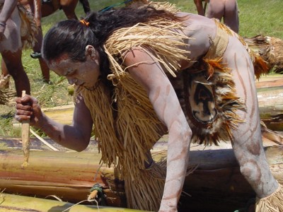 Man met lichaamsbeschildering en traditionele kleding voert een ritueel uit tijdens een festival.