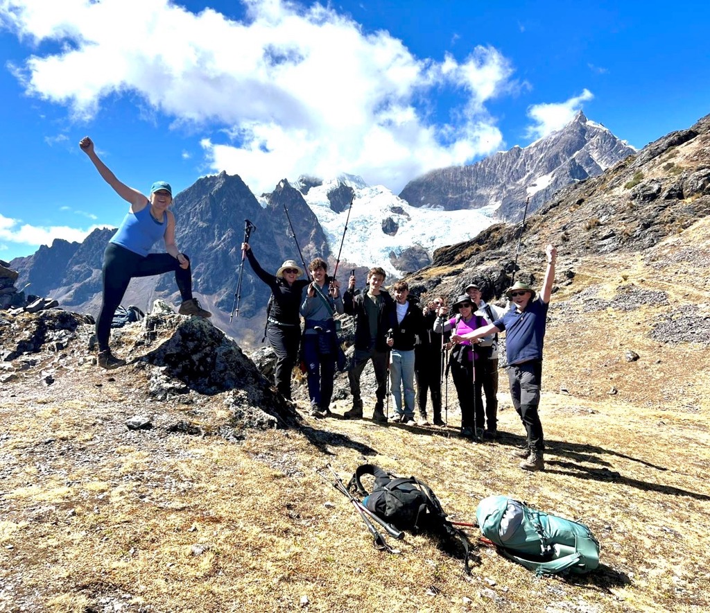 Gezin wandelt in de Andes in Peru met trekkingstokken, met besneeuwde bergtoppen op de achtergrond.
