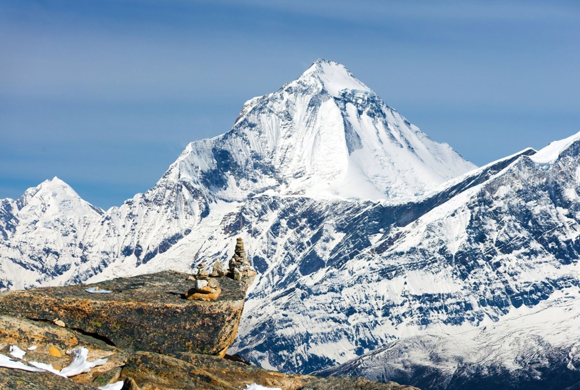 Besneeuwde bergtop in de Himalaya in Nepal, met stenen cairns op een rots op de voorgrond.