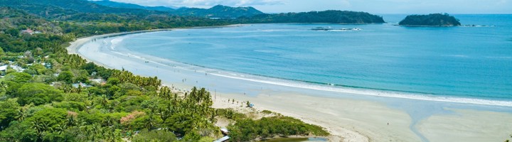 Panoramisch uitzicht op het strand van Sámara, Costa Rica, met palmbomen, baai en helderblauwe zee.