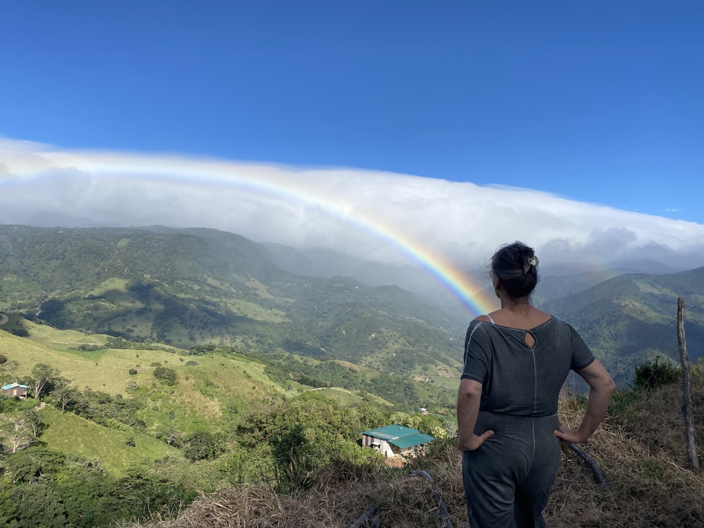 Reiziger kijkt uit over groene bergen langs de Pan-American Highway in Guatemala, met een regenboog aan de hemel.