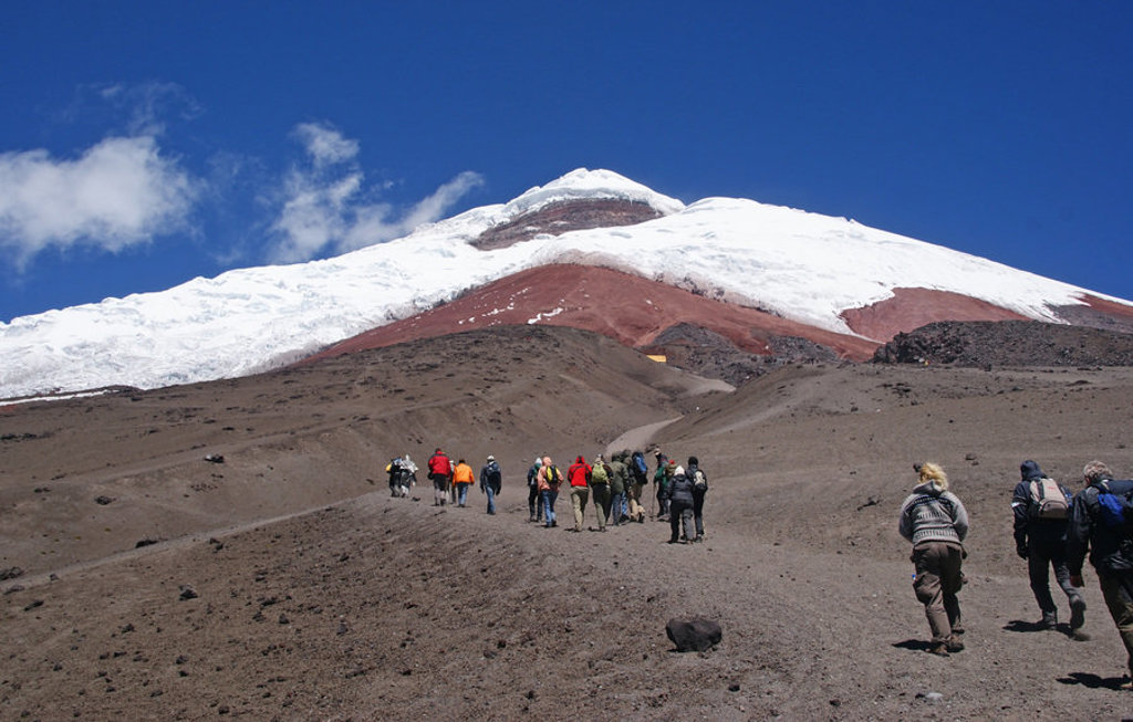 Wandelaars op de flanken van de Cotopaxi-vulkaan in Ecuador, met besneeuwde top onder een blauwe lucht.