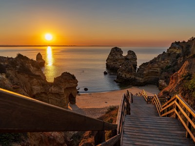 Zonsondergang boven de rotsformaties en het strand van Lagos in de Algarve, met houten trap naar beneden.