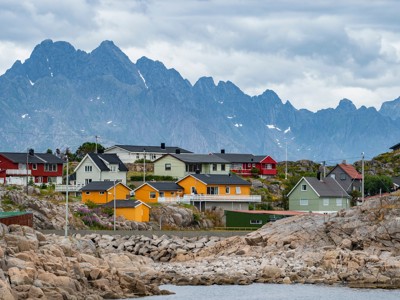 Kleurrijke huizen op de Lofoten aan de rotskust, met ruige bergen op de achtergrond.