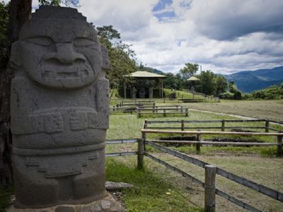 San Agustín-beeld in archeologisch park, Route Colombia, met bergen en wolkenlucht op de achtergrond.