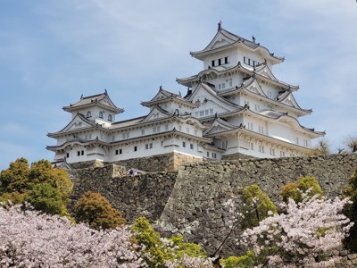 Himeji-kasteel in Japan, wit kasteel op stenen muren met bloeiende kersenbloesem.