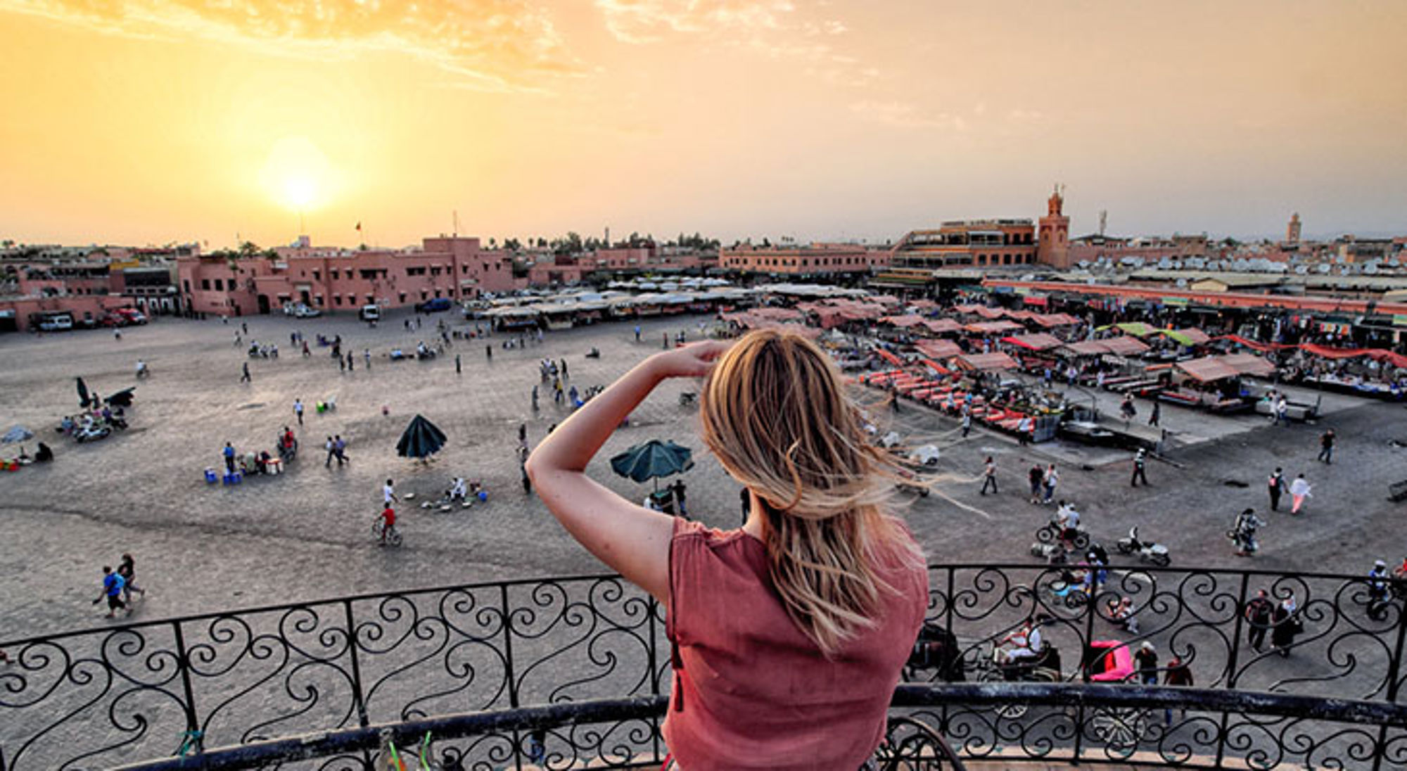 Uitzicht op het Jemaa el-Fna plein in Marrakech bij zonsondergang, met marktkramen en bezoekers.