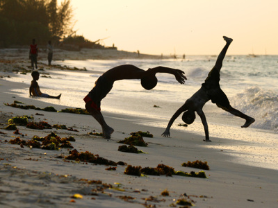 Kinderen maken salto’s op het strand bij zonsondergang tijdens de Route Oost-Afrika.