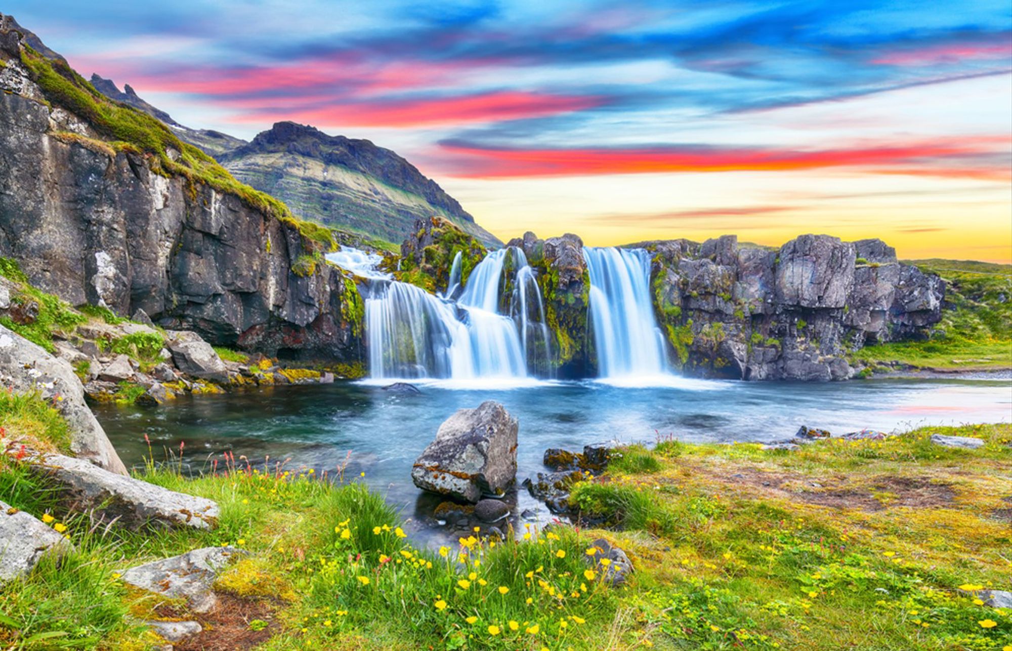 Waterval in IJslands berglandschap bij zonsondergang, met rotsen, groen mos en helder water.