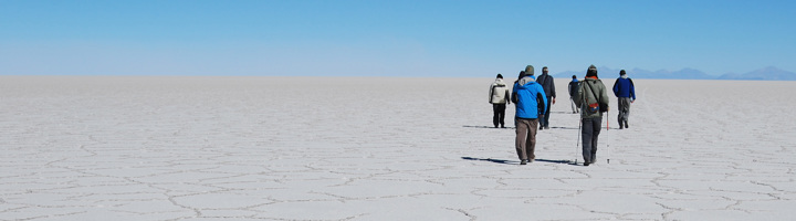 Groepsrondreis Bolivia: reizigers wandelen over de zoutvlakte Salar de Uyuni onder een heldere blauwe lucht.