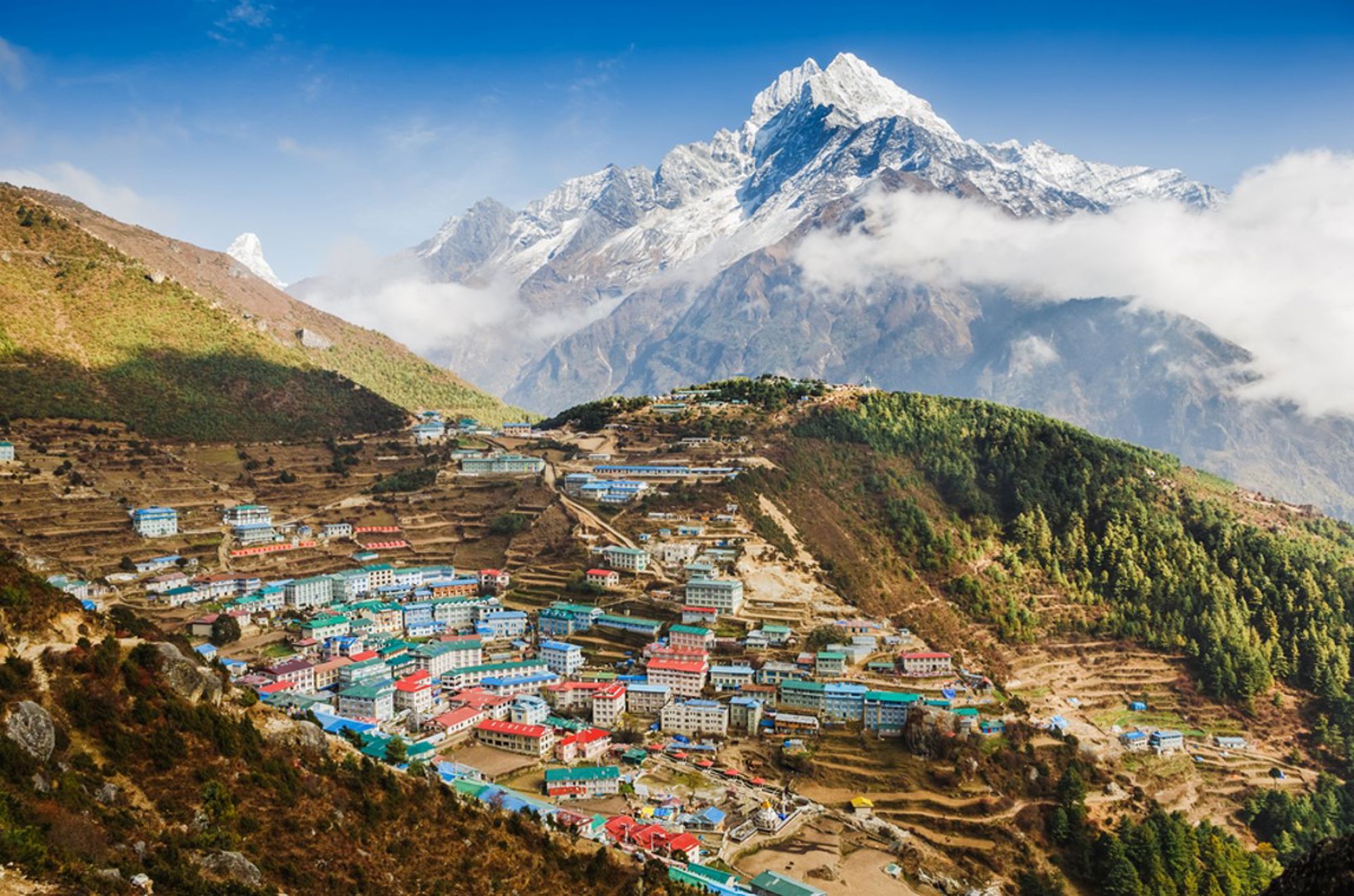 Kleurrijk bergdorp in Nepal met terrassen en besneeuwde Himalaya-toppen op de achtergrond.