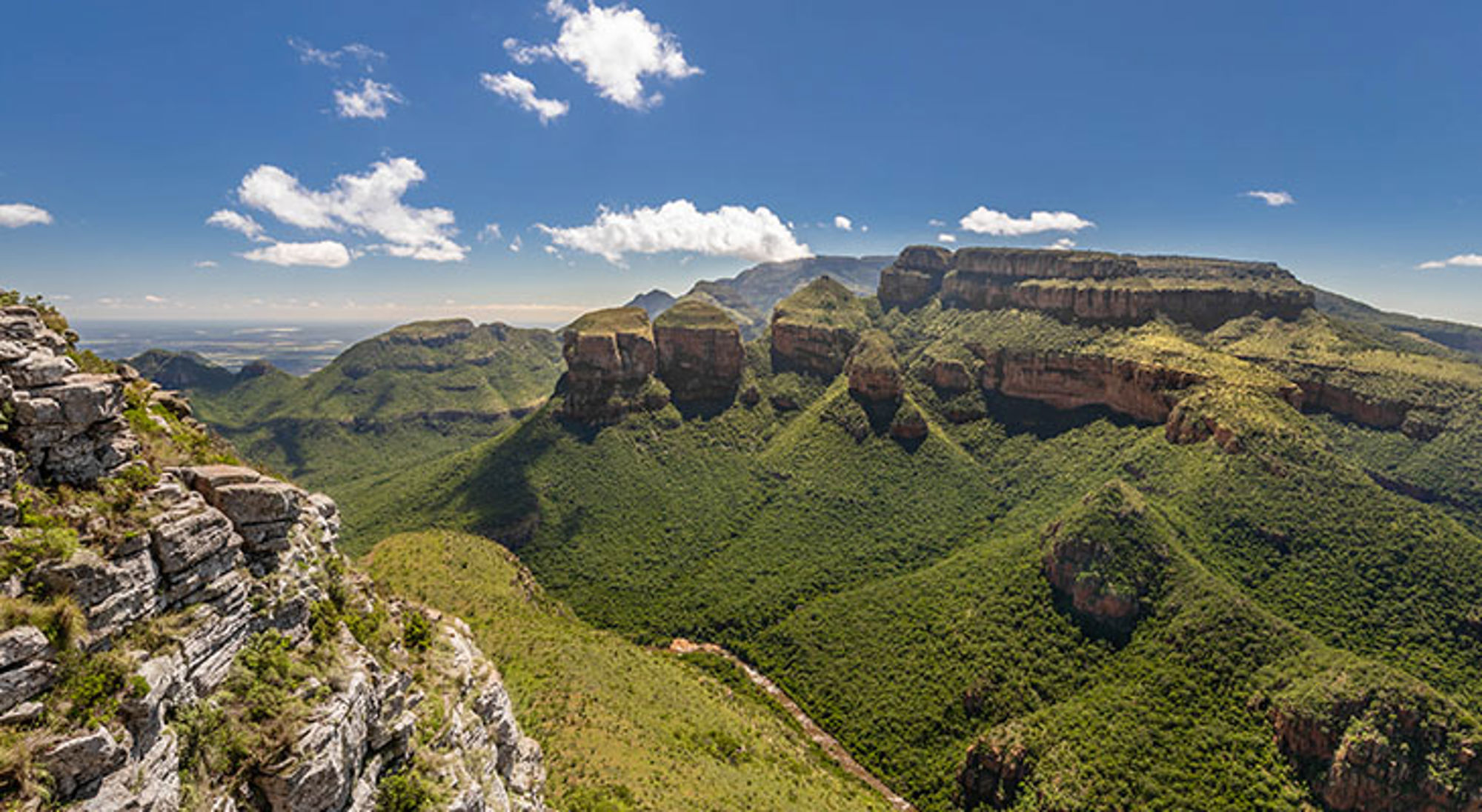 Uitzicht op de Drie Rondavels Uitzicht op de Drakensbergen met groene valleien en rotsplateaus onder een blauwe lucht, Zuid-Afrika.