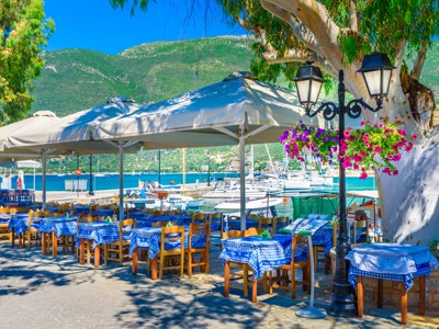 Terras aan de haven in Griekenland met zeilboten en bergen op de achtergrond.